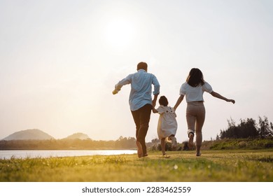 Happy family in the park sunset light. family on weekend running together in the meadow with river Parents hold the child hands.health life insurance plan concept. - Powered by Shutterstock