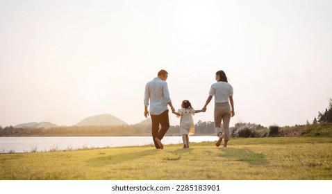 Happy family in the park sunset light. family on weekend running together in the meadow with river Parents hold the child hands.health life insurance plan concept. - Shutterstock ID 2285183901