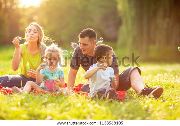 Happy family in the park together on a sunny day – cute children blow soap bubbles outdoor
