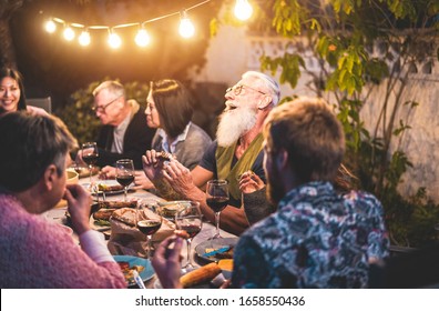 Happy family people having fun at barbecue dinner - Multiracial friends eating at bbq meal - Food, friendship, gathering and summer lifestyle concept - Focus on hipster man left hand