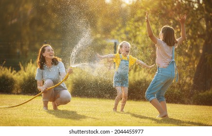 Happy family playing in backyard. Mother sprinkling her kids in hot summer day.