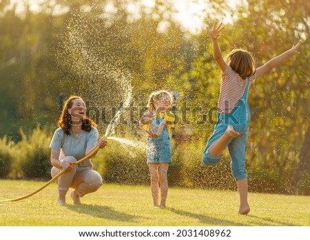 Happy family playing in backyard. Mother sprinkling her kids in hot summer day.