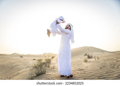 Happy family playing in the desert of Dubai -  Playful father and his son wearing traditional arab clothing having fun outdoors - Powered by Shutterstock