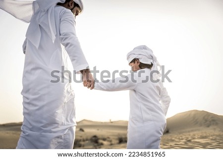 Happy family playing in the desert of Dubai -  Playful father and his son wearing traditional arab clothing having fun outdoors