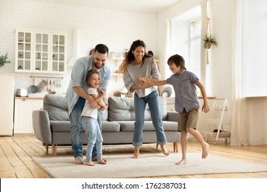 Happy family playing funny game having fun together with little son and daughter in modern living room. Young dad and mother with adorable cute children doing exercises, enjoying weekend at home. - Shutterstock ID 1762387031