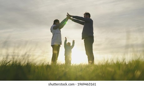 Happy Family Playing With Little Daughter, Family Symbol At Home In Sun. Mom Is Dad And They Depict With Their Hands Roof Of House Over Head Of Child. Dream Of A Shared Home. Home Builders