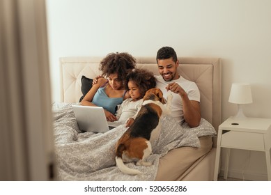 Happy family playing with their dog in bed. - Powered by Shutterstock