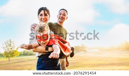 Happy family playing together outside - Kid in a superhero costume having fun with mother and dad in the park at sunset - Family, love and childhood concept	