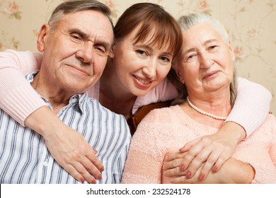 Happy Family. Portrait Of Elderly Couple And Adult Daughter Happily Looking At Camera. Senior Man, Woman With Their Caregiver At Home.