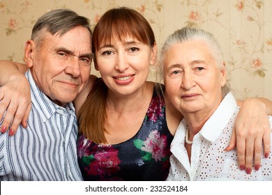 Happy Family. Portrait Of Elderly Couple And Adult Daughter Happily Looking At Camera. Senior Man, Woman With Their Caregiver At Home.