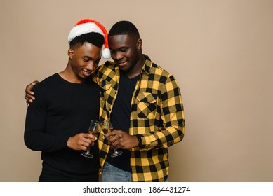 Happy Family Portrait On Christmas, Gay Male Couple On Beige Background. A Pair Of Black Men In Love Clink Glasses Of Champagne. Cheers. Celebrate Christmas And New Year