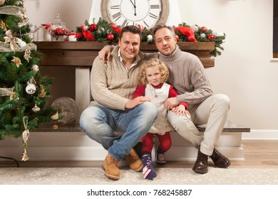 Happy Family Portrait On Christmas, Gay Male Couple And One Child Sitting Near Fireplace At Home, Chritmas Decoration Around Them