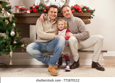 Happy Family Portrait On Christmas, Gay Male Couple And One Child Sitting Near Fireplace At Home, Chritmas Decoration Around Them