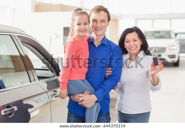 Happy family posing together near their newly\
bought car at the dealership copyspace Asian woman smiling holding\
car keys posing with her husband and daughter after buying a new\
auto transport owners 