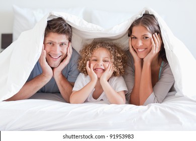 Happy family posing under a duvet while looking at the camera - Powered by Shutterstock