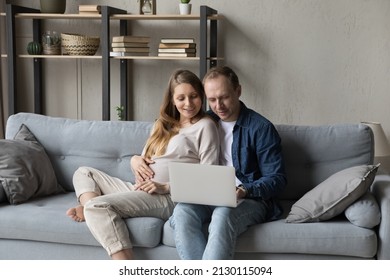 Happy family pregnant couple relaxing on comfortable couch together, using computer, shopping with online ecommerce app on laptop, browsing Internet, talking on video call, touching big belly - Powered by Shutterstock