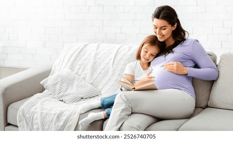 Happy family pregnant mother and preschooler daughter spending time together at home, reading book - Powered by Shutterstock