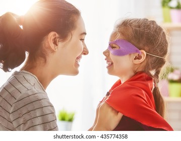 Happy family is preparing for a costume party. Mother and her child girl playing together. Girl in Superman's costume.  - Powered by Shutterstock