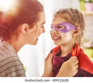 Happy family is preparing for a costume party. Mother and her child girl playing together. Girl in Superman's costume.  - Powered by Shutterstock