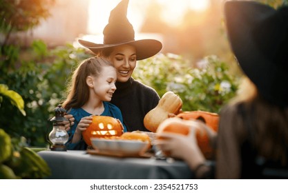 Happy family preparing for Halloween. Mother and children carving pumpkins in the backyard of the house.