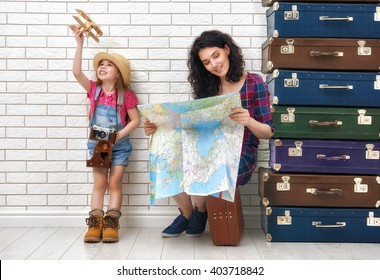 Happy Family Preparing For The Journey. Mother And Daughter Looking At A Map And Choose A Country To Travel.