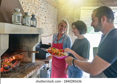 Happy family preparing meal together  with beef skewers cooking on the barbecue in the chimney