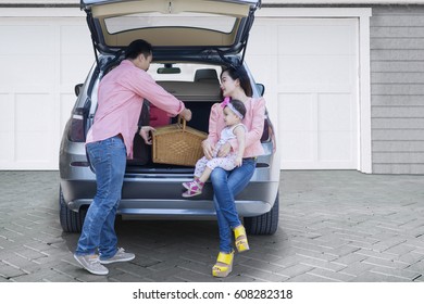 Happy Family Preparing Suitcase And A Picnic Basket Into A Car For Holiday