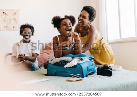 Happy family preparing for a vacation, laughing together as they pack travel essentials. Parents, along with their excited daughter, enjoy  planning and getting ready for a fun-filled holiday.