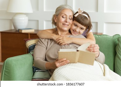 Happy family pretty elderly female grandma or babysitter reading template book to cute little child girl. Smiling granddaughter embracing grandmother telling funny fairy tale story sitting on sofa. - Powered by Shutterstock