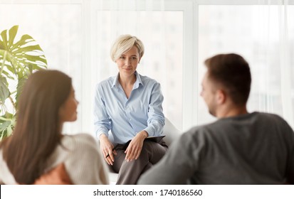 Happy Family Psychologist Smiling Looking At Couple's Reconciliation During Therapy Session Sitting In Office. Selective Focus