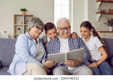 Happy family reading a book at home. Grandparents and children reading stories together. Smiling grandfather, grandmother and little kids sitting on the couch and looking at the book together - Powered by Shutterstock