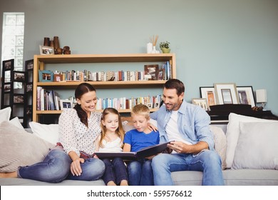 Happy Family Reading Book While Sitting On Sofa At Home