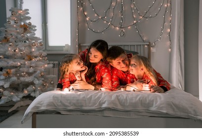 A Happy Family In Red Christmas Pajamas Are Lying In A Cozy Bed In The Morning.