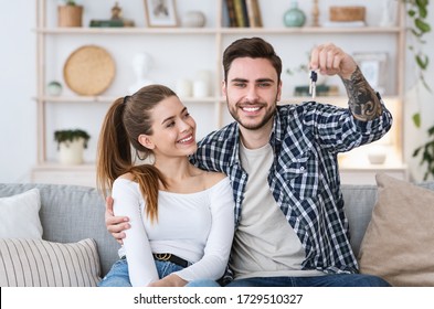 Happy family rejoice in new apartment. Guy with girl sitting on sofa and holding keys.