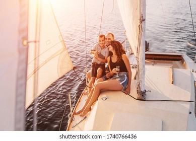 Happy Family Relaxing On Sailboat At Sunset