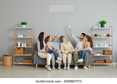 Happy family relaxing on sofa under newly installed or serviced air conditioner in modern home interior. Young parents, kids, senior grandparents adjusting AC and enjoying new cold warm mode settings