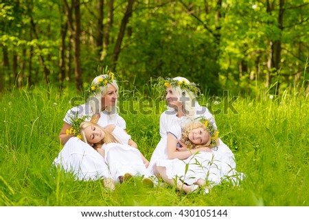 Happy family resting on the nature in the summer. Mom and daughter with wreath in the flowers in the park. Girls sitting in the park on the grass