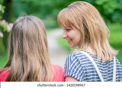 Happy Family Resting Together - Mother And Daughter Walking In Park At Summer Or Spring Day. Beautiful Woman Talking To  Teen Girl And Smiling. Outdoors Portrait - Back View.