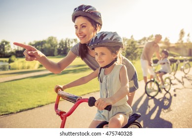 Happy family is riding bikes outdoors and smiling. Parents are teaching their children. Mom and daughter in the foreground