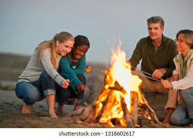 Happy Family Roasting Marshmallows Over A Bonfire On A Beach.