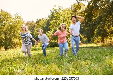 Happy family running hand in hand across a meadow in summer in nature - Shutterstock ID 2256557003