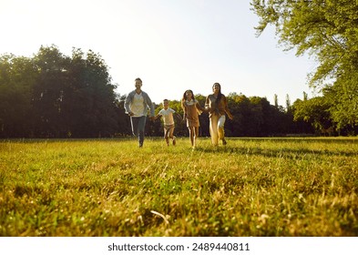 Happy family running and having fun in summer park enjoying sunny day in nature. Mother, father and their cheerful two children boy and girl walking on green grass outdoors at sunset together. - Powered by Shutterstock