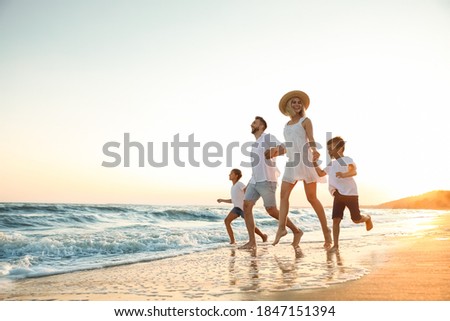 Happy family running on sandy beach near sea at sunset