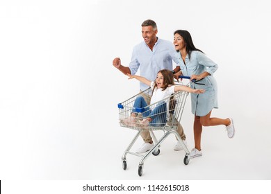 Happy family runnnig while shopping together with a supermarket trolley, little daughter sitting in a trolley isolated