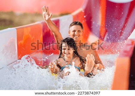 Happy family rushes down high slide on an inflatable circle in water park. Father and daughter in aquapark.