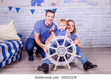 Happy Family In Sailor T-shirts Playing With Steering Wheel Indoors. Travel And Adventure Concept. Studio Shoot