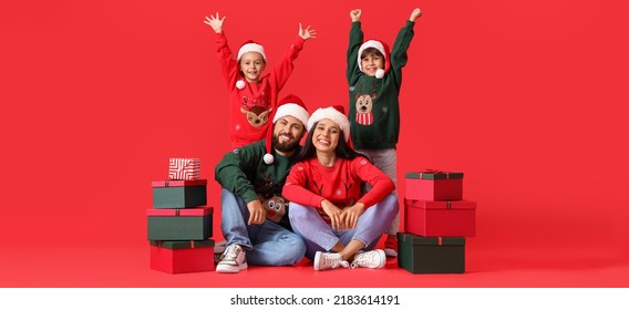 Happy family in Santa hats and with Christmas gifts on red background - Shutterstock ID 2183614191