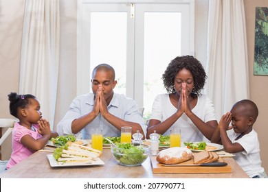 Happy family saying grace before meal at home in the kitchen - Powered by Shutterstock