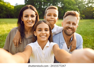 Happy family selfie in summer park. Parents and children having fun together. Pretty Caucasian european girl holds camera and takes photo of beautiful mother, handsome father and cute little brother - Powered by Shutterstock