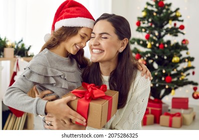 Happy family sharing joy with each other on Christmas. Mother receives gifts from her loving child on Xmas Day. Smiling daughter gives present to mommy in living room with decorated tree in background - Powered by Shutterstock